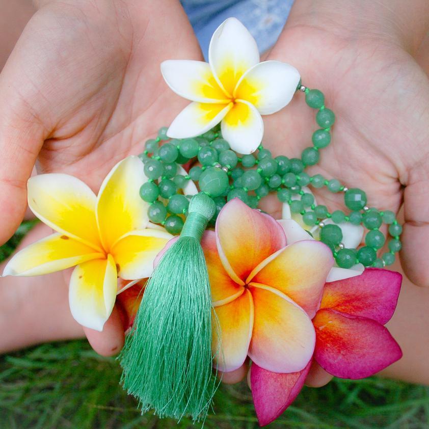 Green Aventurine Gemstone Mala Beads with tassel held in palms of hand with plumeria flowers - Yoga Jewelry - Blooming Lotus Jewelry
