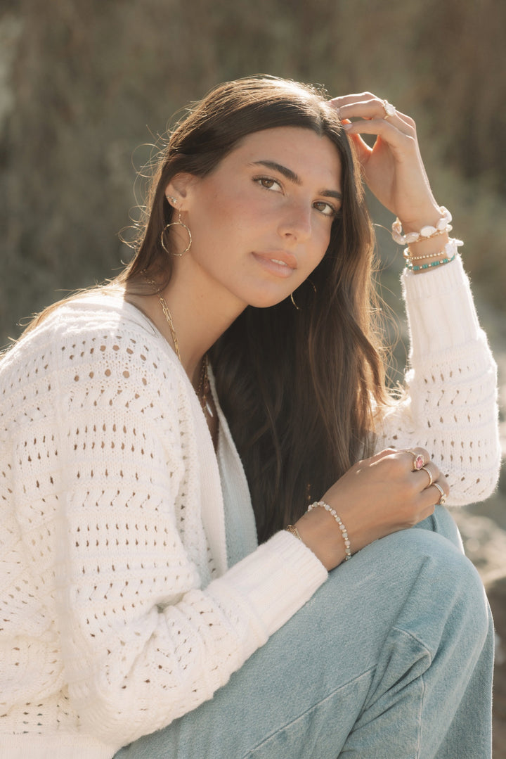 Woman wearing gold hoops, studs, and gemstone bracelets in coastal boho style by Blooming Lotus Jewelry.