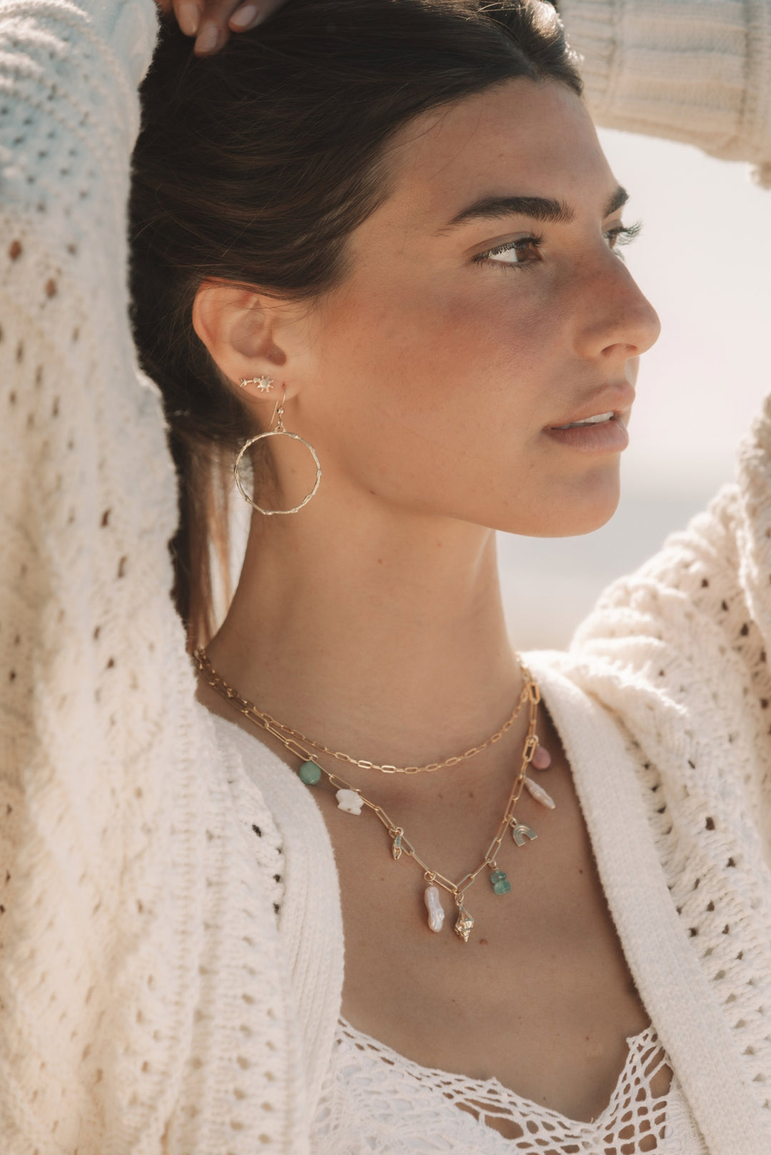 woman wearing gold hoop earrings and layered gemstone charm bar necklace in a coastal boho style by Blooming Lotus Jewelry.