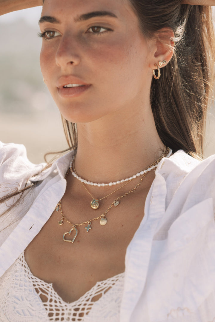 Woman with sun-kissed skin wearing layered tiny branch twig hoops, gold charm necklaces and pearl choker by Blooming Lotus Jewelry.