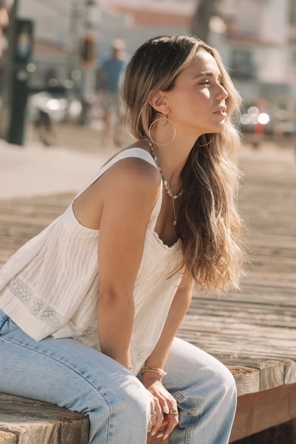 Model wearing large gold Olive Branch Hoops and layered gemstone and gold necklaces by Blooming Lotus Jewelry, coastal boho style at the beach.