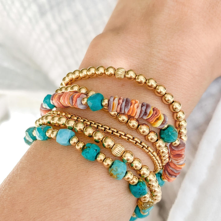 gold beaded stacking bracelets with shells and turquoise cubed beads on wrist close up