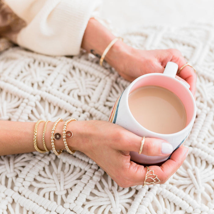 Gold beaded layering braclets on model holding coffee mug - Blooming Lotus Jewelry