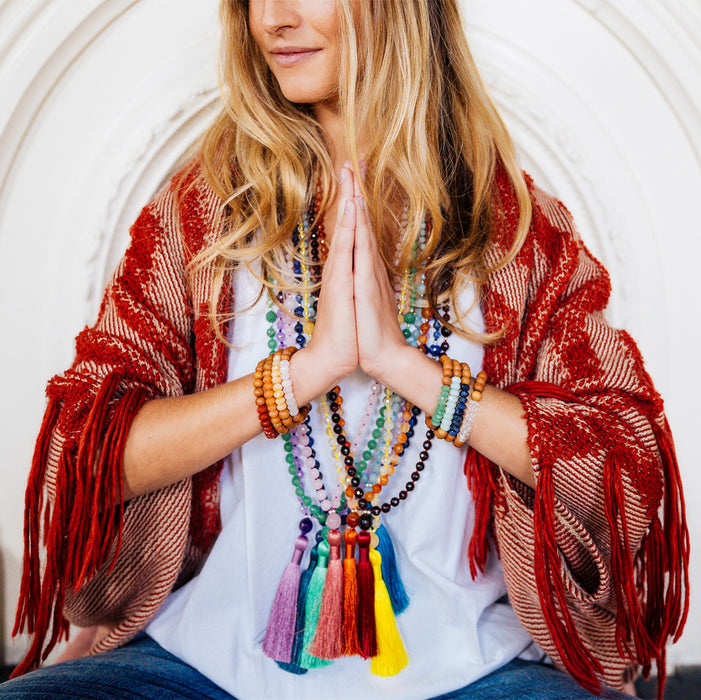 several boho gemstone mala beads necklaces with tassels on yoga model with hands in prayer namaste