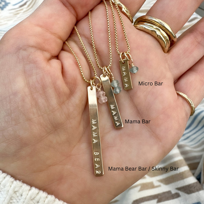 three gold bar necklaces personalized with words and gemstones in palm of hand