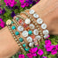 gold beaded bracelets with gemstones and personalized white alphabet beads on models wrist with flowers in background