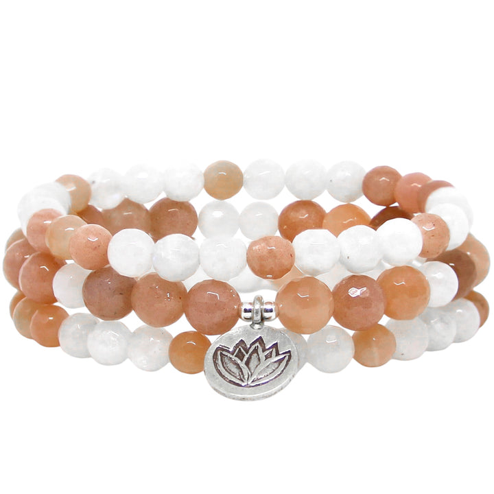 A yoga-inspired gemstone bracelet stack featuring alternating white and peach moonstone beads, accented with a silver lotus charm. There are 3 bracelets, displaying a warm, earthy color palette. The polished gemstone beads are round and faceted, reflecting light.