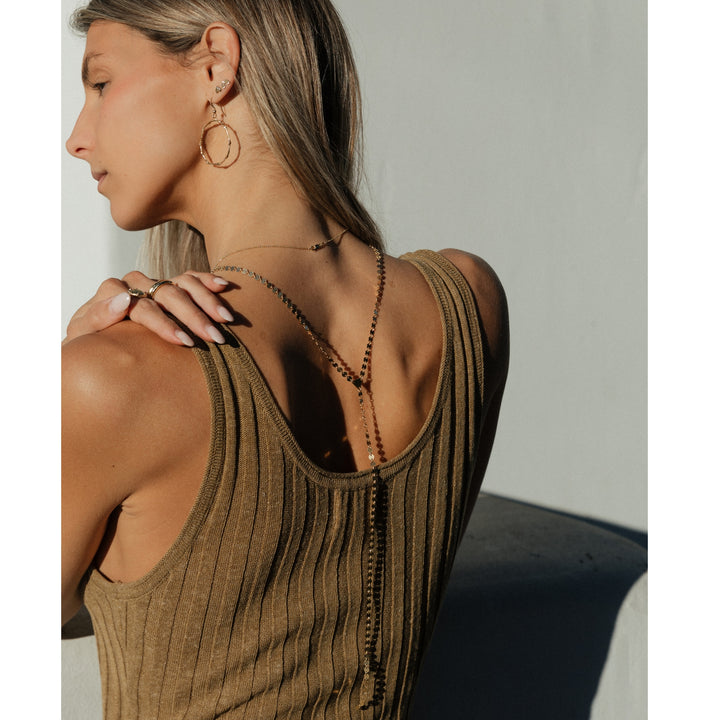 Back view of woman wearing the Sol Lariat Necklace by Blooming Lotus Jewelry, styled with branch gold hoops, tiny studs, and stacking rings. The Y-shaped necklace drapes gracefully down her back, catching the light.