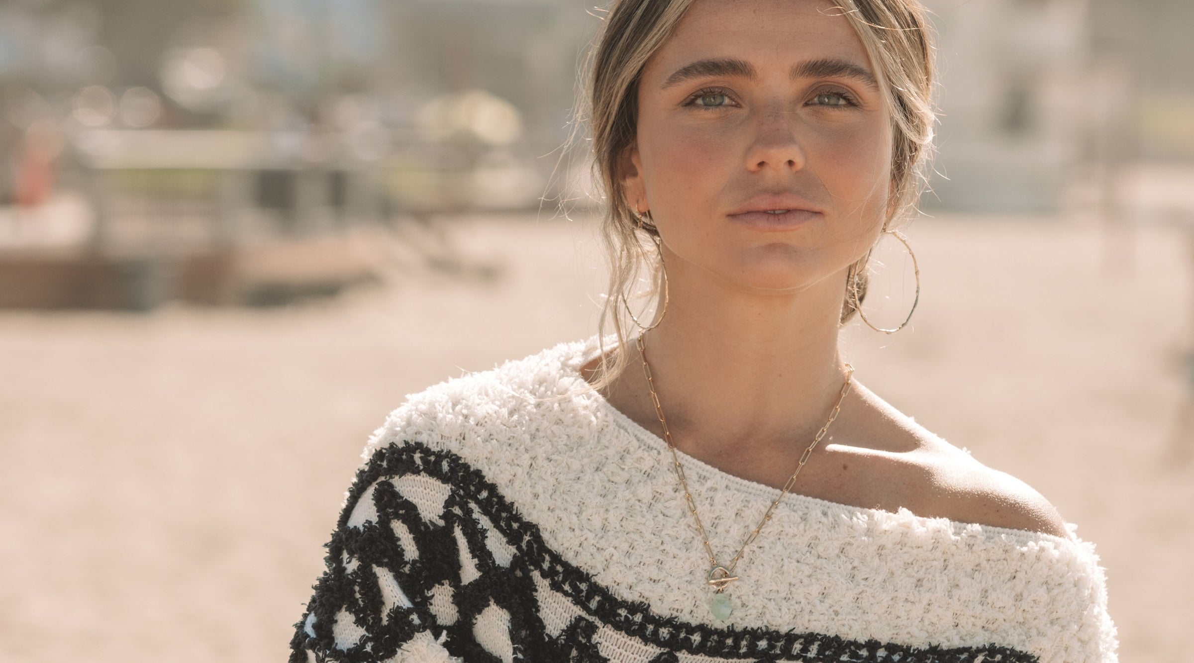 Woman wearing coastal-inspired gold and gemstone jewelry at the beach with Black Friday sale text overlay.