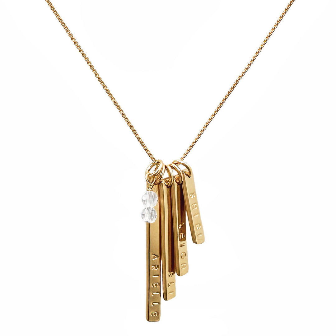 Gold necklace featuring four personalized skinny bar charms hand-stamped with names and accented by clear quartz gemstones — meaningful keepsake jewelry by Blooming Lotus Jewelry.