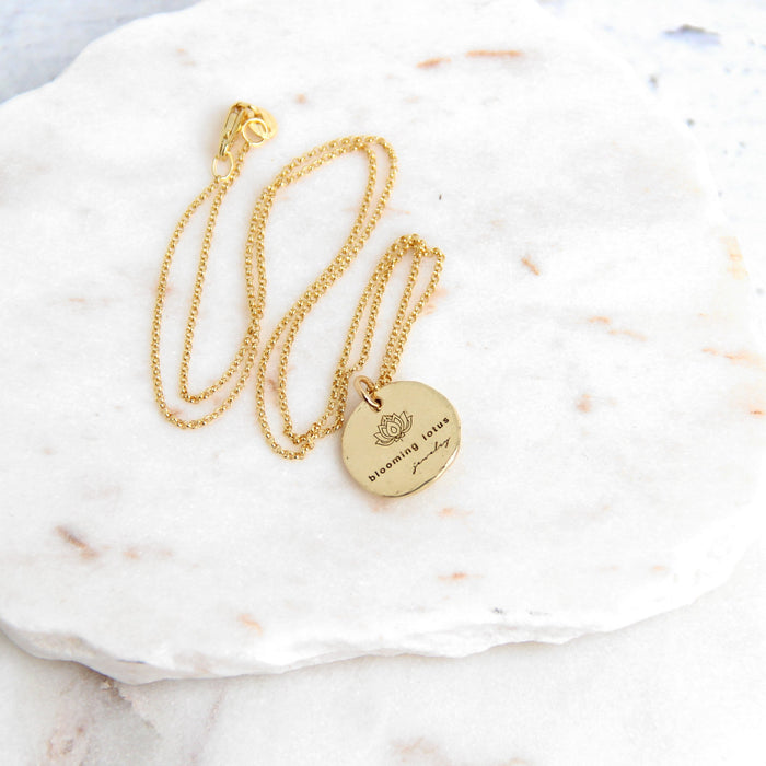 Blooming Lotus Jewelry maker's mark logo on backside of gold pendant on marble slab
