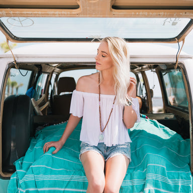 boho mala beads necklace on model sitting on turquoise towel in back of a volkswagon bus