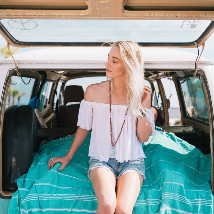 boho mala beads necklace on model sitting on turquoise towel in back of a volkswagon bus
