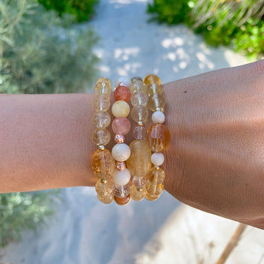 4 Citrine Rutilated Quartz Gemstone bracelets on wrist with sand and plants in background 