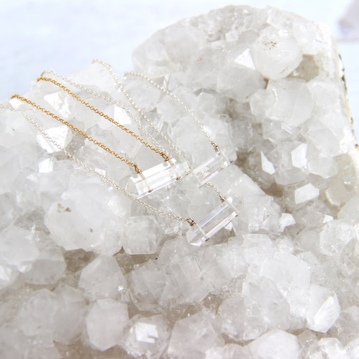 three clear quartz crystal point necklaces on silver and gold chain laying on top of apophyllite crystal cluster
