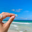 Silver Mantra Ring engraved with LET GO held between index and thumb with blue sky beach and ocean in background