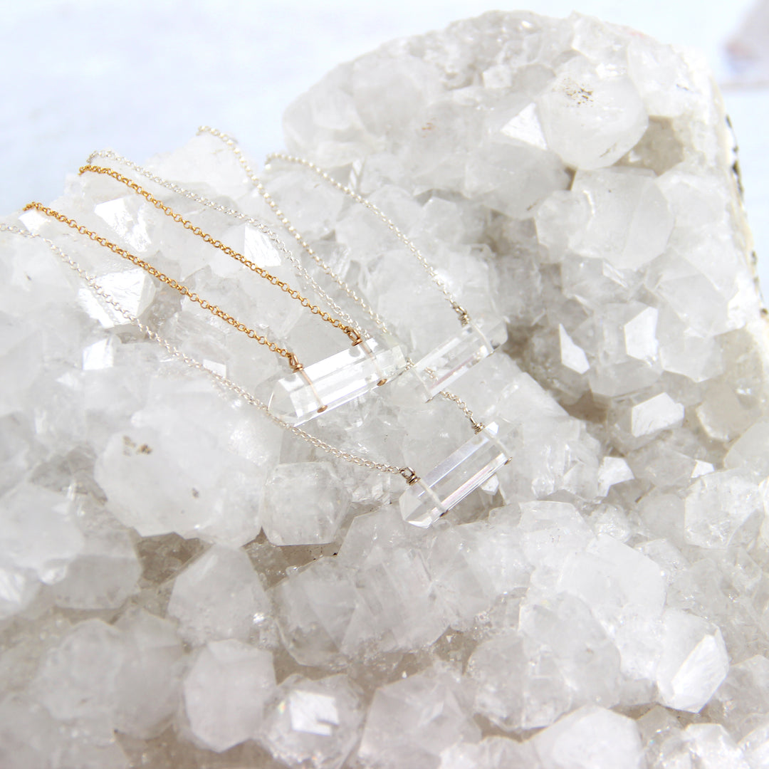 clear quartz crystal pendant necklaces displayed on natural quartz cluster, boho healing stone jewelry in gold and silver