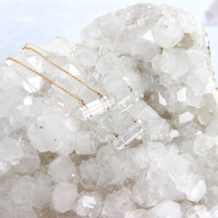 clear quartz crystal pendant necklaces displayed on natural quartz cluster, boho healing stone jewelry in gold and silver