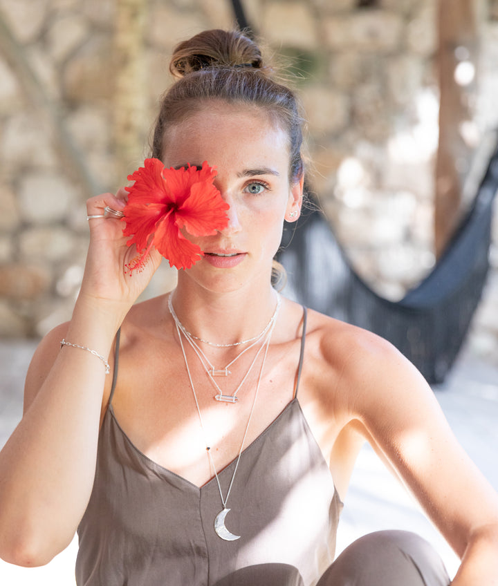 layered clear quartz double terminated necklace worn by woman holding red hibiscus flower, boho coastal jewelry with healing crystal meaning