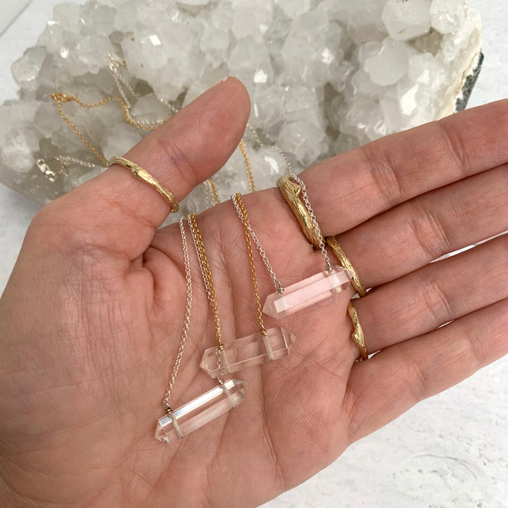 hand holding clear quartz crystal pendant necklaces, double terminated healing stone jewelry in gold and silver