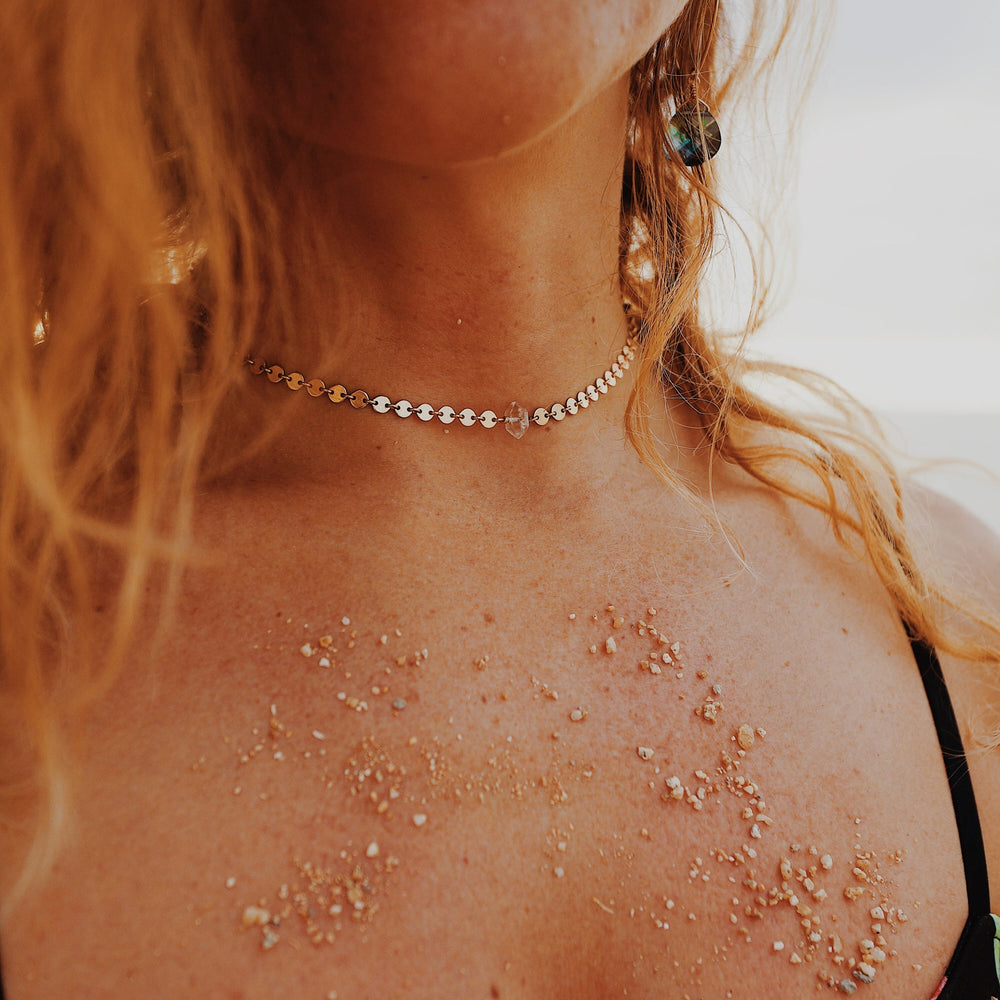 Woman wearing a gold-filled Herkimer Diamond choker necklace with a natural clear quartz crystal pendant and sun-kissed beach-inspired styling.